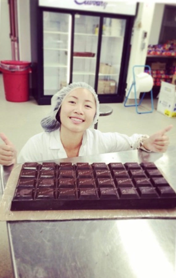 Jennifer smiling with thumbs up behind a giant tray of Cadbury chocolate in a production kitchen